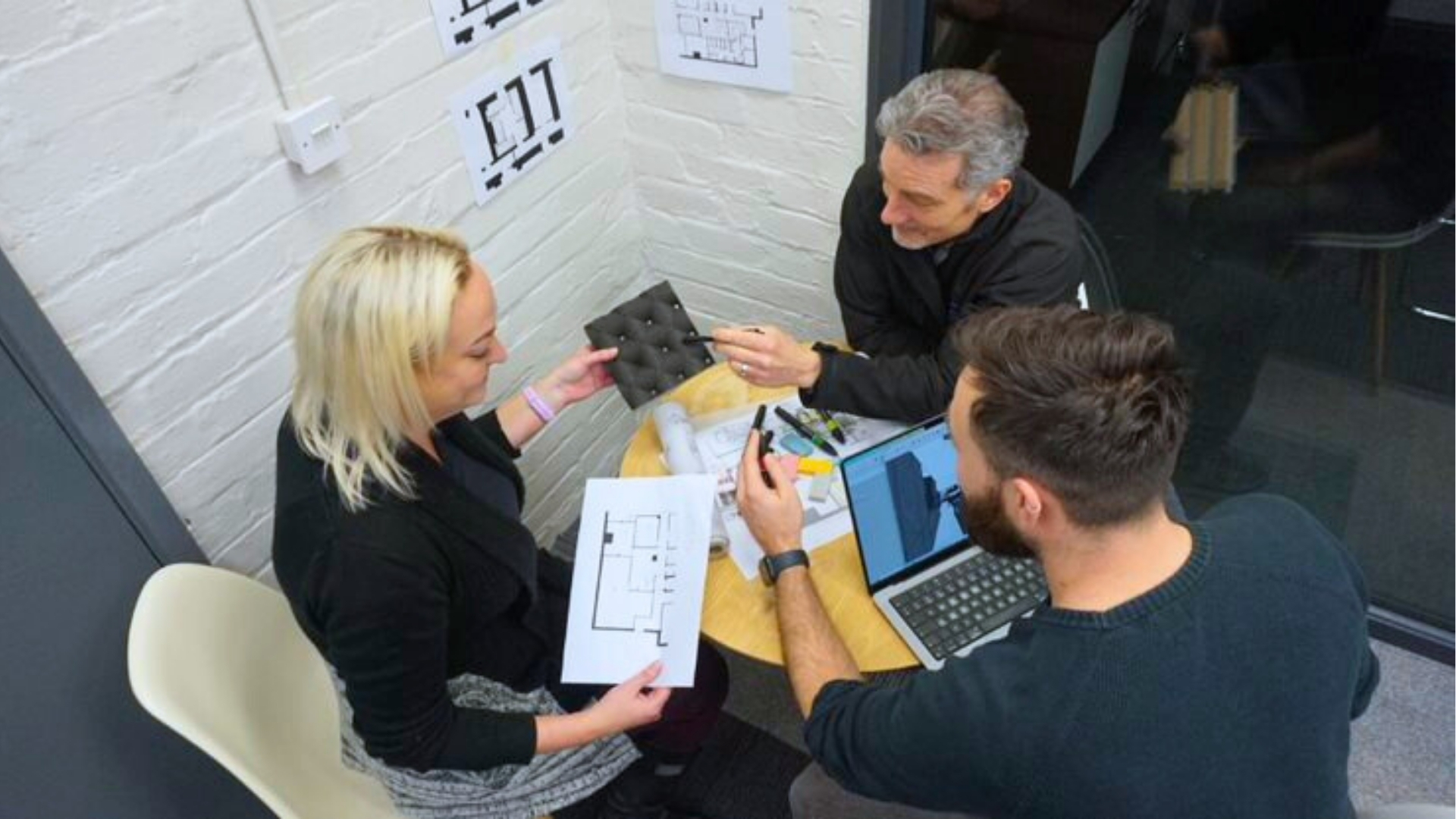 Three Ripple team members sit around a table reviewing floor plans, 3D renders, and material samples during a design meeting.